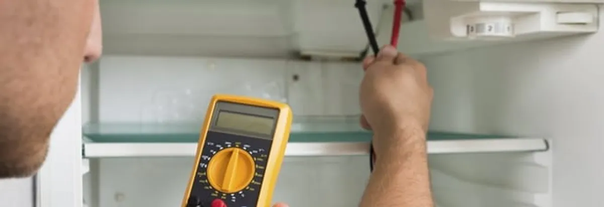 Refrigerator repair technician testing electrical components with a multimeter in Worcester, MA