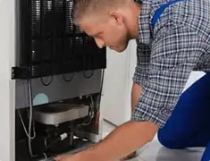 Refrigerator repair technician servicing the compressor and condenser area in Worcester, MA